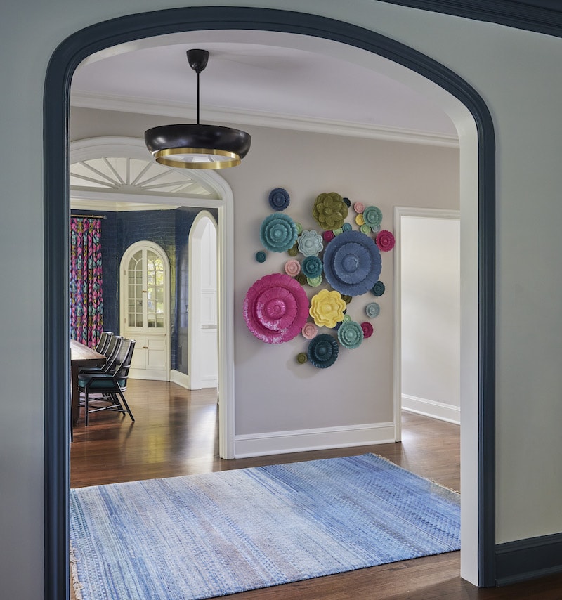 Chicago Interior Design: A captivating arched entryway framed in deep blue leads to a hallway adorned with vibrant floral wall accents. The dining space, defined by arched doors, features deep blue walls and boldly patterned curtains, all accentuated by subtle wood flooring and a blue-patterned rug.