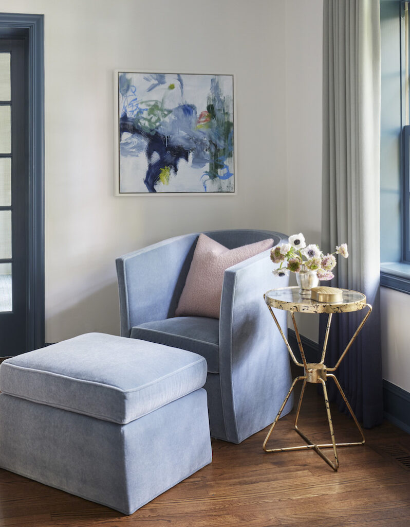 Room corner designed by chicago interior designer featuring a beautiful blue arm chair with a matching footrest and a baby pink cushion. The setup includes a gold-gilded sculptural side table and contemporary artwork on the wall, creating a cohesive furniture arrangement
