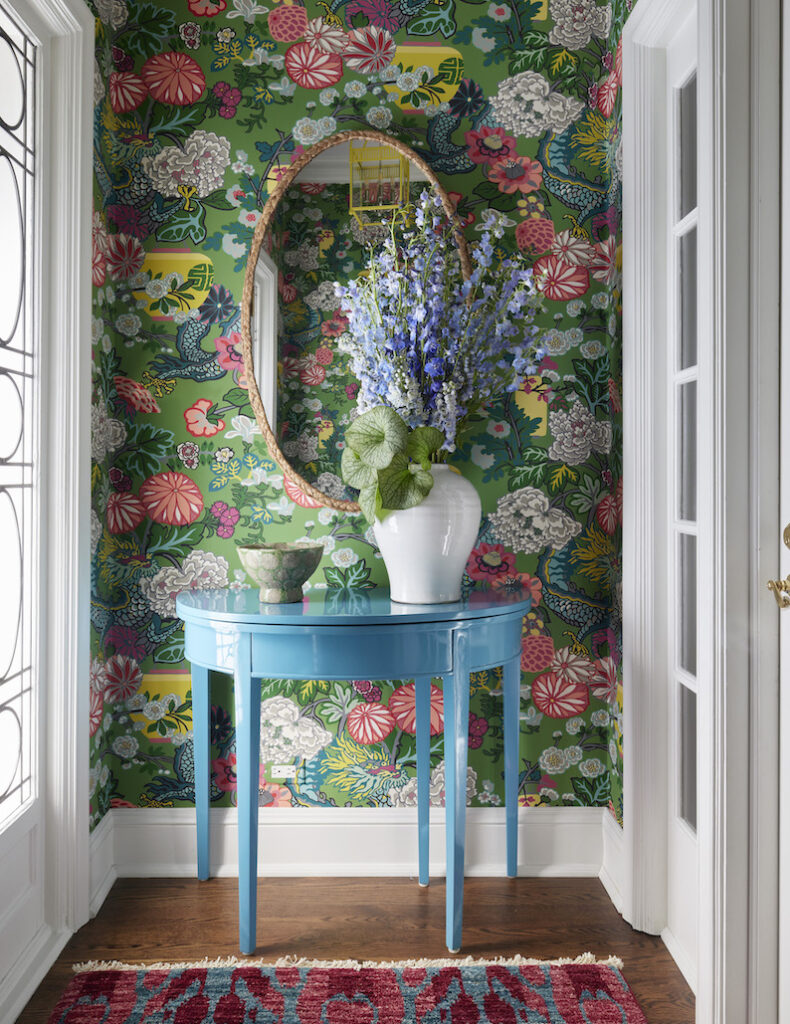 Colorful interior design project: A vibrant entryway featuring white walls and a striking floral wallpapered accent wall. A bold blue semi-circular console serves as a centerpiece, adorned with accent decor against the vivid backdrop