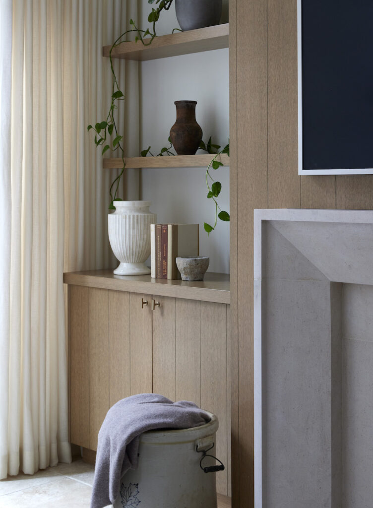 A vignette featuring a minimalist mantle, accompanied by a simple wooden bookshelf and long sheer drapes adorning the windows