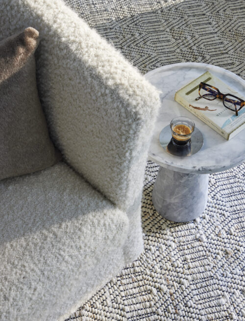 Boucle chair and patterned rug with marble side table holding a cup of coffee