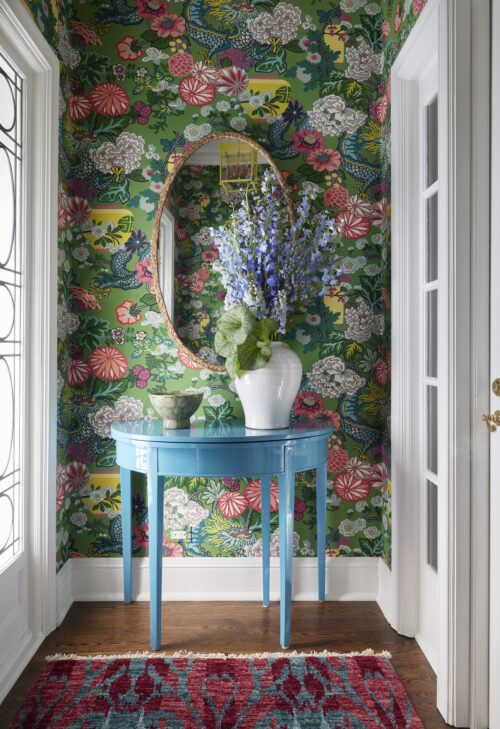 Entryway with floral wallpaper, large blue flowers, a white vase, and a bright blue end table