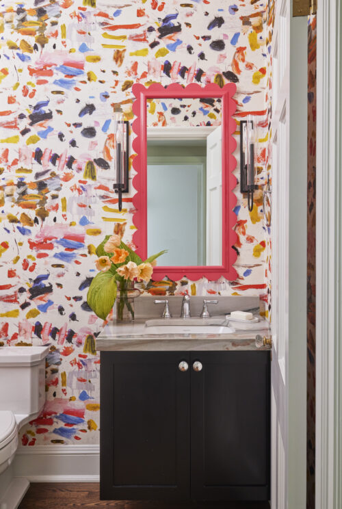 Powder room with pink scalloped mirror and patterned wallpaper