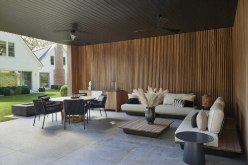 Outdoor living and dining room with wood-paneled walls and neutral-toned furniture