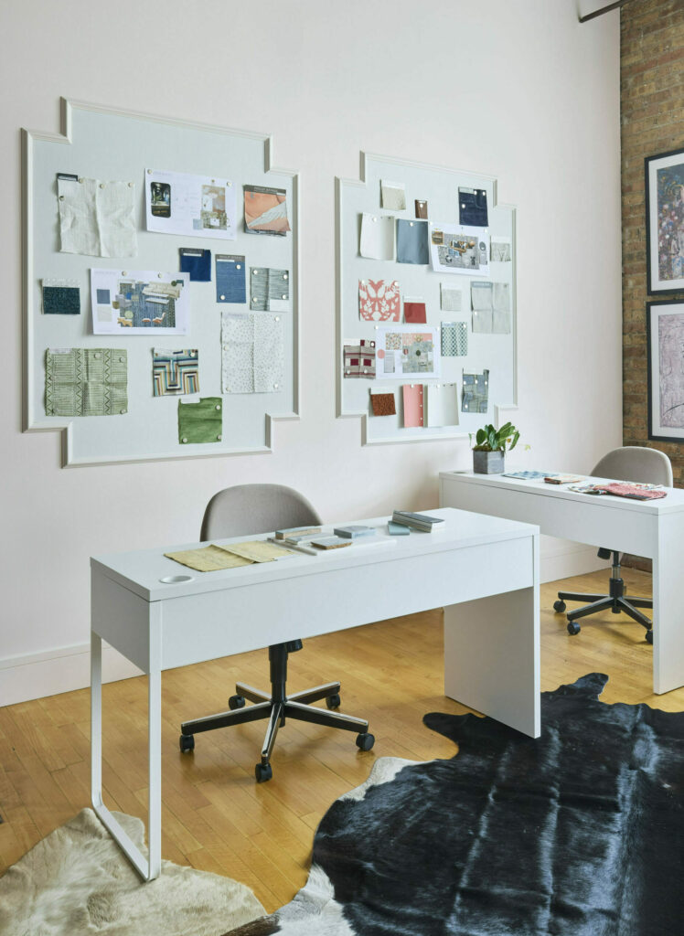 Interior design studio featuring two desks, two chairs, wall art, and fabric samples