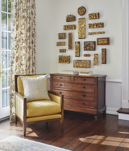 A living area featuring a yellow chair, artifacts on the wall, and a wooden console