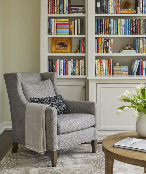 An at-home library featuring custom bookshelves, a gray armchair, and cozy decor accessories