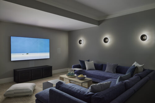 An at-home movie theater featuring a large blue sectional couch, TV screen, and wall sconces