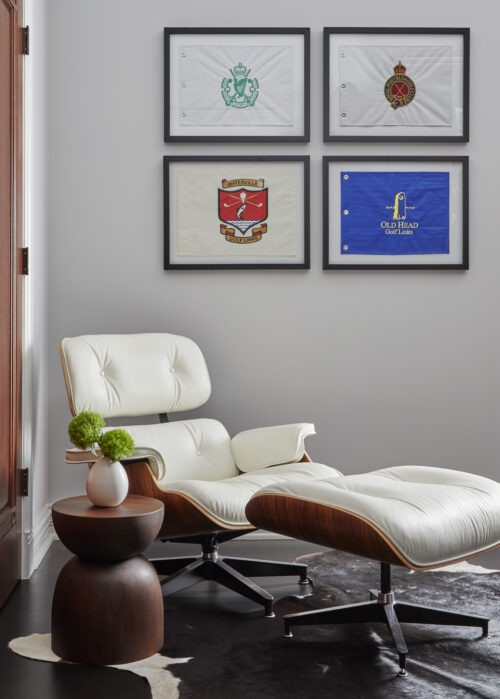 A cozy home corner featuring a white lounge chair, framed golf flags, and a wooden side table