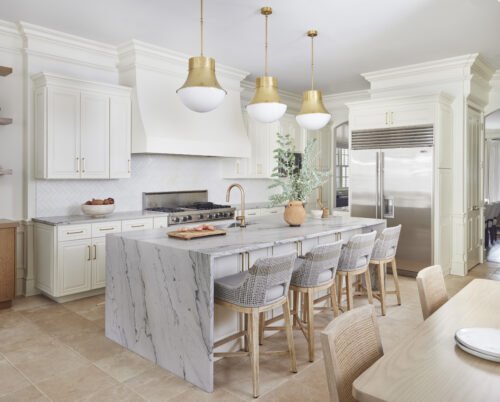 Luxury kitchen with marble island, gold light fixtures, and white cabinetry.