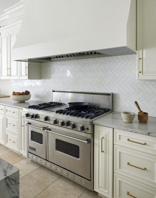 Luxury kitchen with custom stove hood, stove and oven, and gold hardware.