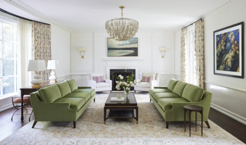 Living room with green sofas, patterned rug, art, and a gold chandelier.