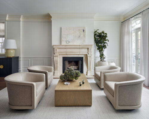 Living room with light wood coffee table, fireplace, minimalist art, and tan armchairs.