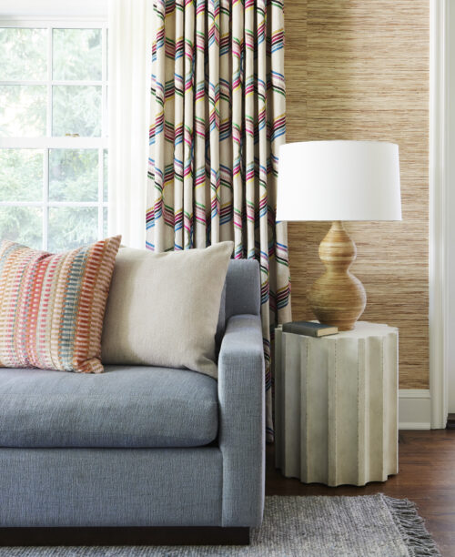 Living room with blue sofa, patterned drapery, throw pillows, and a funky side table.