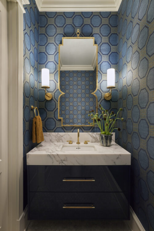 Powder room featuring blue patterned wallpaper, white marble vanity, and a funky mirror.