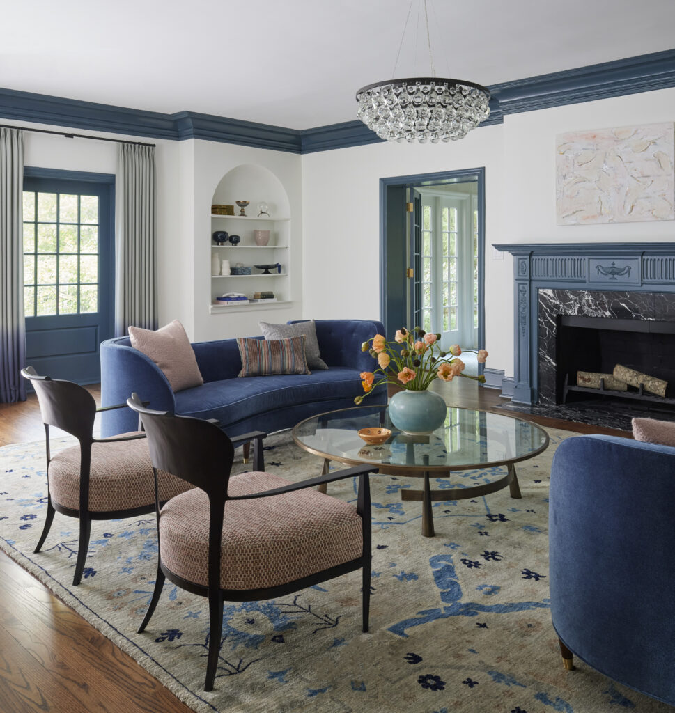 Living room with blue sofa, wooden upholstered armchairs, a custom fireplace, and blue trim.