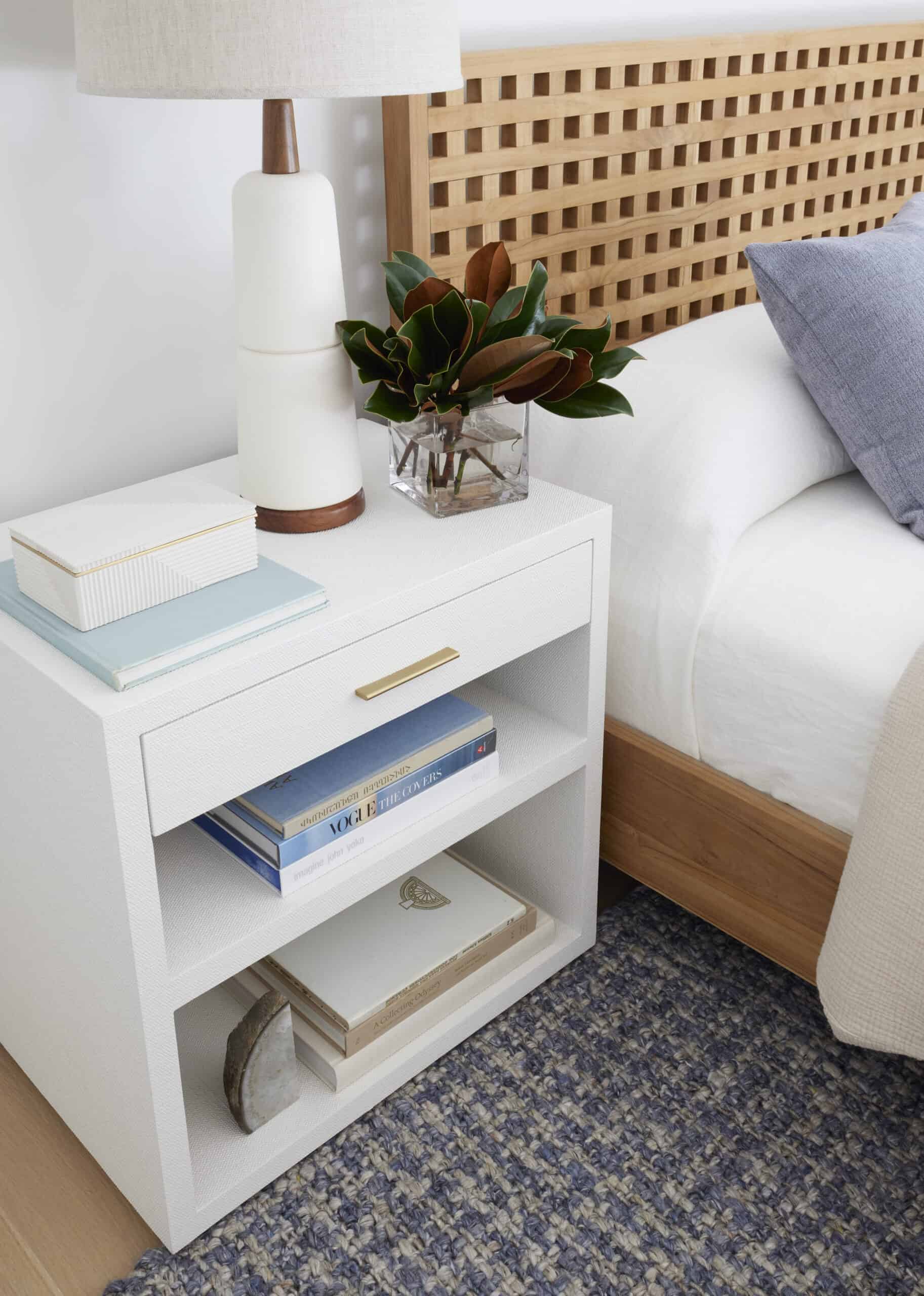 Nightstand with lamp, plant, and books next to bed